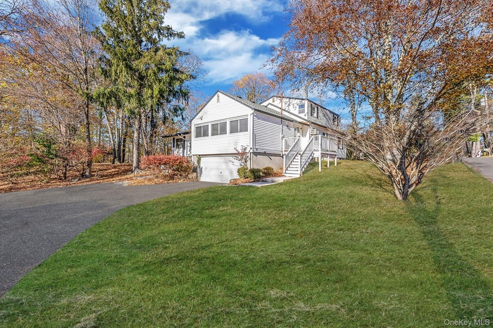 View of home's exterior with asphalt driveway, a sunroom, a lawn, a garage, and stairs