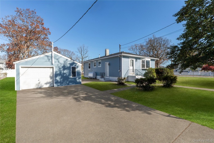 View of front facade featuring a front lawn, an outbuilding, a detached garage, driveway, and oil tank