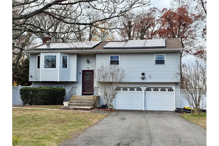 Raised ranch featuring roof mounted solar panels, driveway, an attached garage, and a chimney