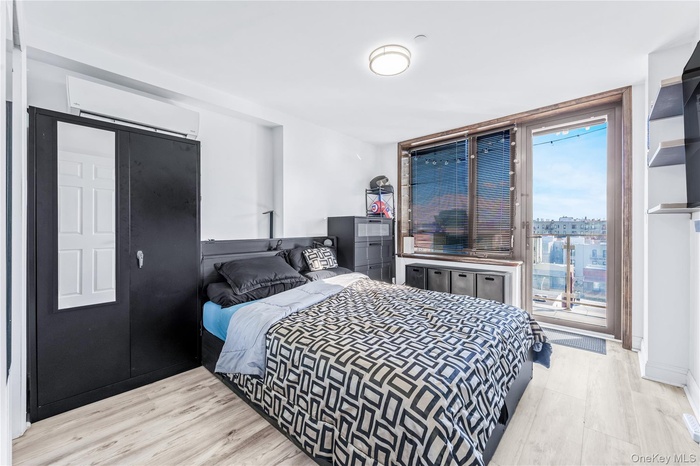 Bedroom featuring light wood finished floors, a wall mounted air conditioner, access to outside, and floor to ceiling windows