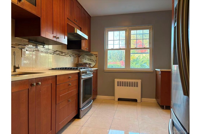 Kitchen with radiator heating unit, appliances with stainless steel finishes, brown cabinets, light countertops, and tasteful backsplash