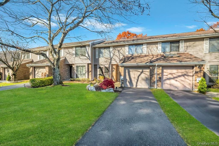 View of front of property featuring driveway, a front yard, brick siding, and an attached garage