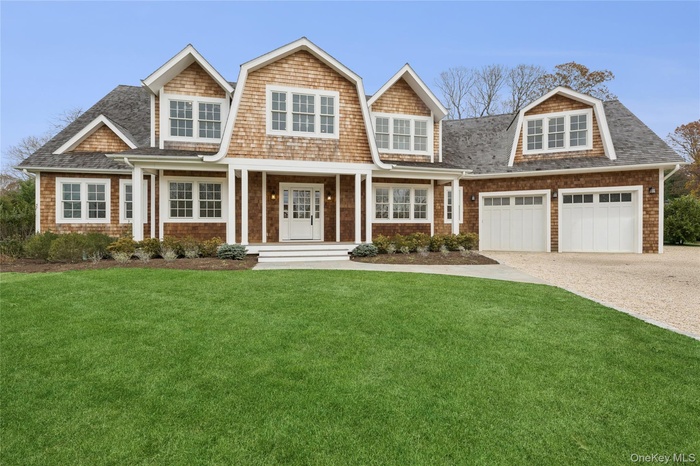 Shingle-style home featuring covered porch, a front yard, a garage, driveway, and a gambrel roof