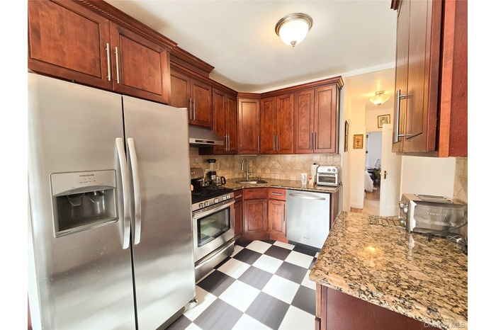Kitchen featuring appliances with stainless steel finishes, dark floors, light stone counters, tasteful backsplash, and under cabinet range hood