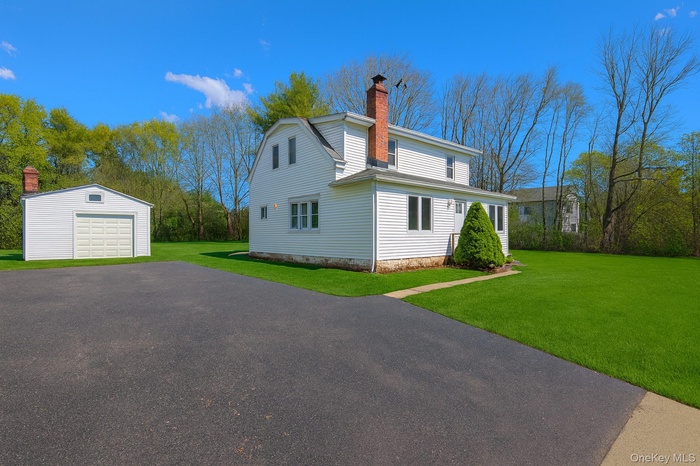 View of side of property featuring a yard, an outbuilding, a chimney, a gambrel roof, and a detached garage