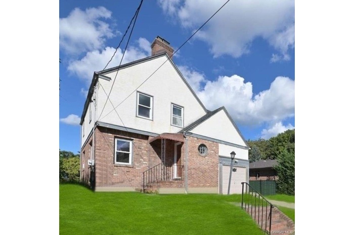 Rear view of house with brick siding, a yard, a chimney, and an attached garage