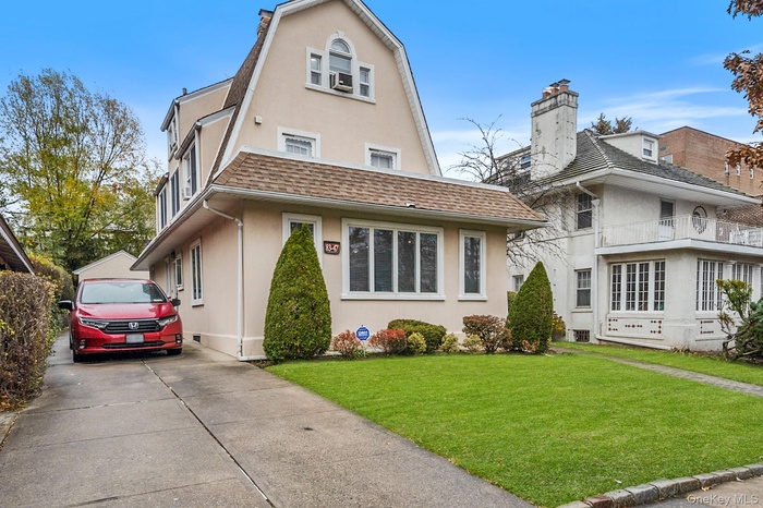 Colonial inspired home with a front yard, stucco siding, a shingled roof, and driveway