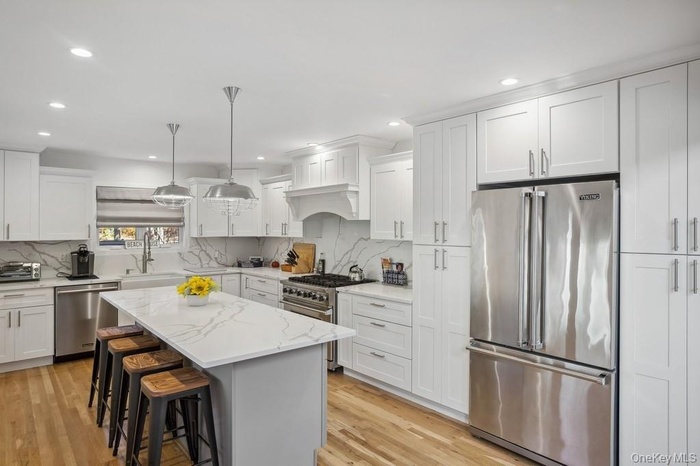 Kitchen featuring white cabinetry, high end appliances, light wood-type flooring, and a sink