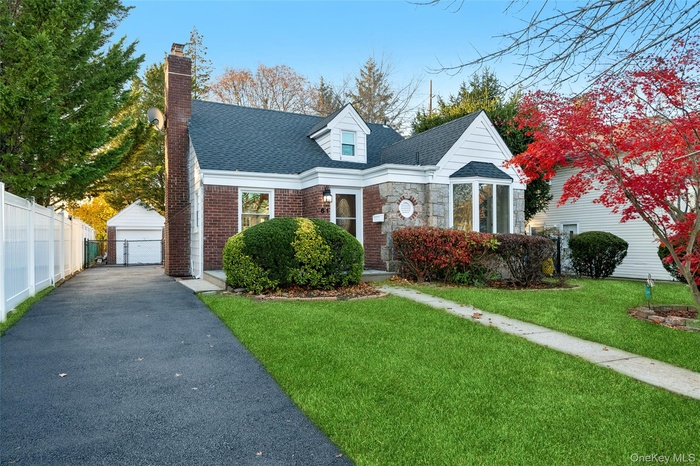 Cape cod-style house with a shingled roof, a detached garage, an outdoor structure, a chimney, and brick siding