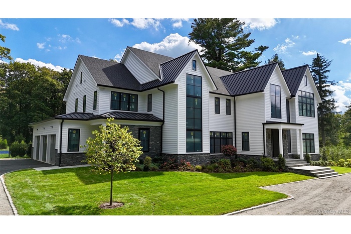 Modern farmhouse featuring a standing seam roof, a metal roof, stone siding, and a front lawn