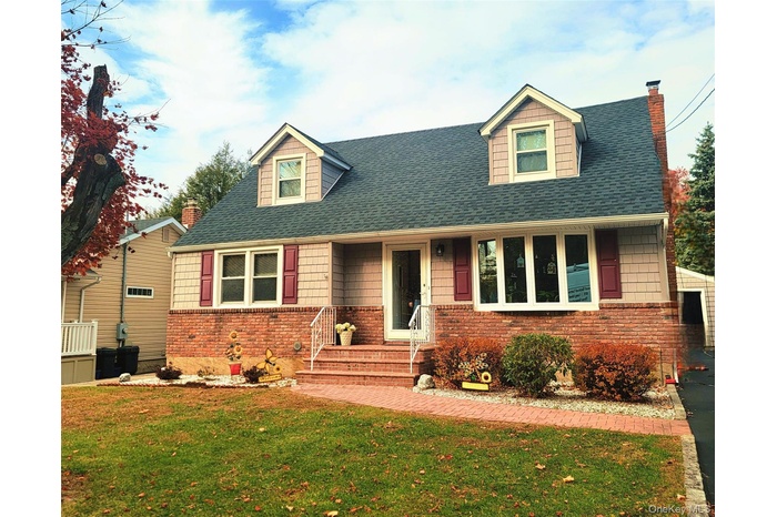Cape cod house with a shingled roof, a chimney, a front yard, and covered porch