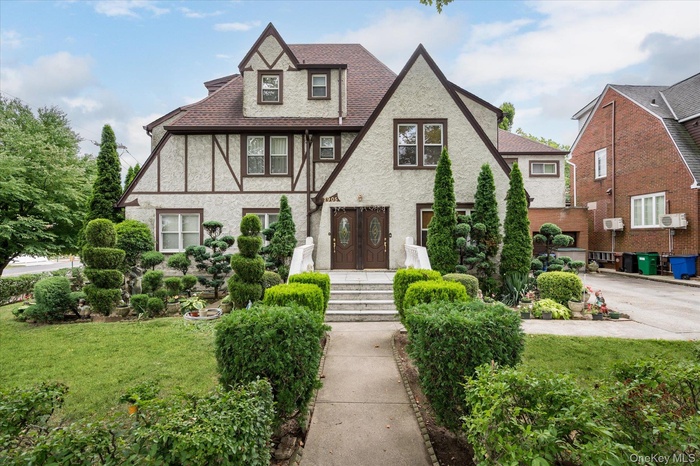 Tudor-style house with a front yard, roof with shingles, and stucco siding