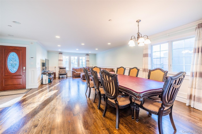 Dining space featuring ornamental molding, a decorative wall, a wainscoted wall, wood finished floors, and a chandelier