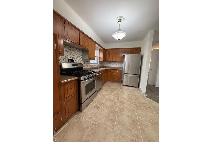 Kitchen featuring stove, fridge, brown cabinets, and hanging light fixtures