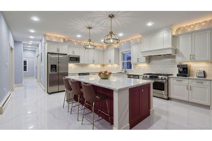 Kitchen featuring stainless steel appliances, recessed lighting, white cabinets, light stone countertops, and hanging light fixtures