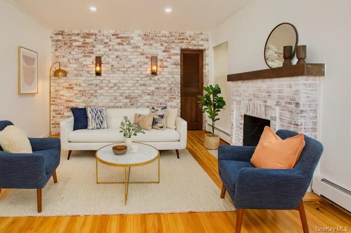 Living room with a baseboard heating unit, brick wall, wood finished floors, a fireplace, and recessed lighting