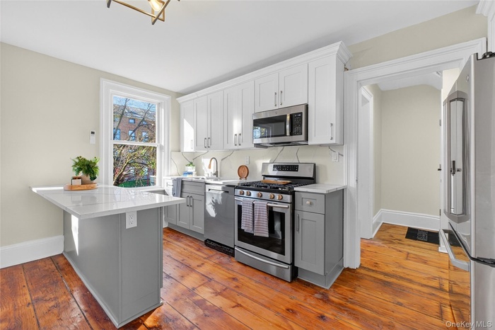 Kitchen with gray cabinets, stainless steel appliances, white cabinetry, and light stone counters