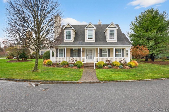 New england style home featuring a chimney, a front yard, and covered porch