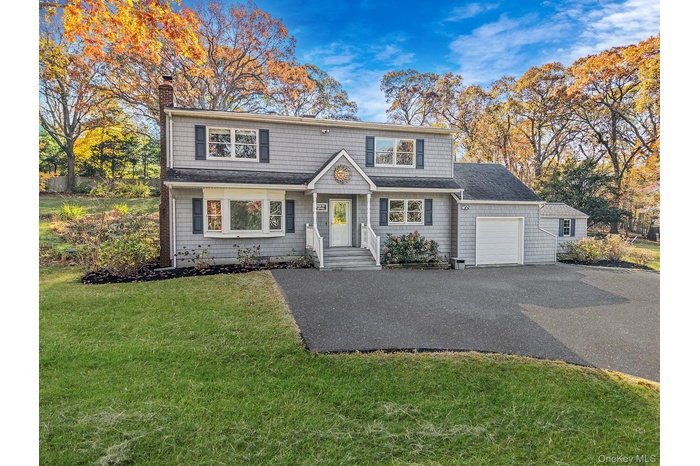 View of front of home featuring a chimney, driveway, a garage, a front lawn, and a shingled roof