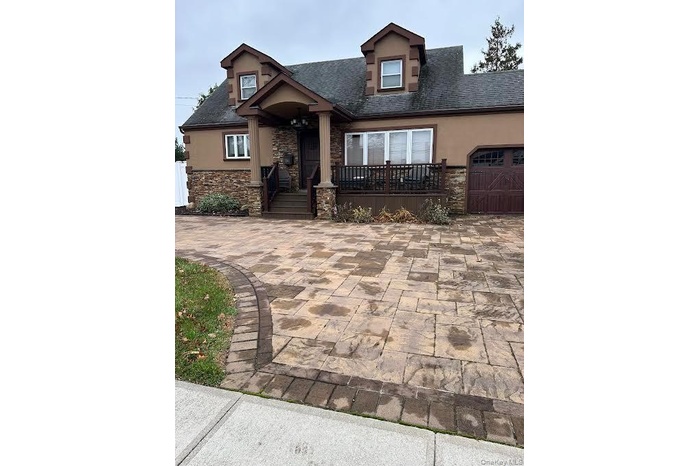 View of front of house featuring stone siding, an attached garage, roof with shingles, and decorative driveway