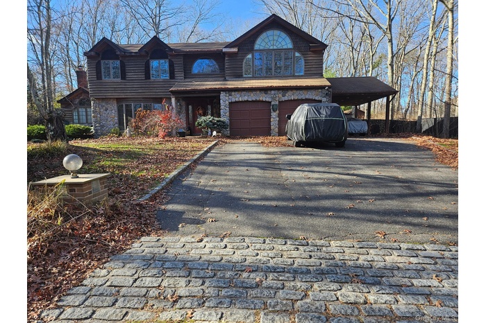 View of front facade featuring stone siding, driveway, and an attached garage