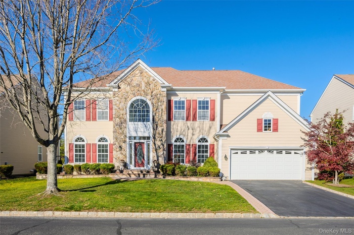 Colonial inspired home with driveway, a front lawn, stone siding, a garage, and roof with shingles