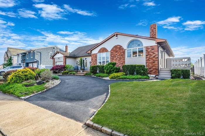 View of front facade featuring brick siding, a chimney, a front yard, and asphalt driveway
