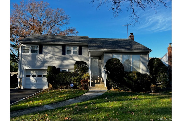 View of front of property with a front yard, a chimney, an attached garage, and asphalt driveway