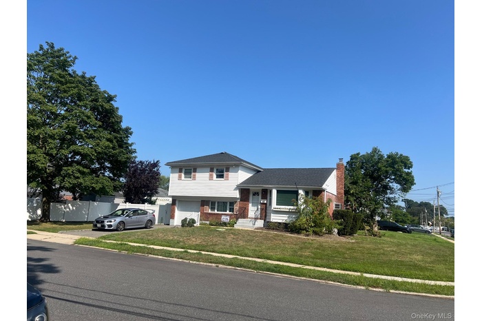 Tri-level home featuring brick siding, a chimney, an attached garage, and driveway