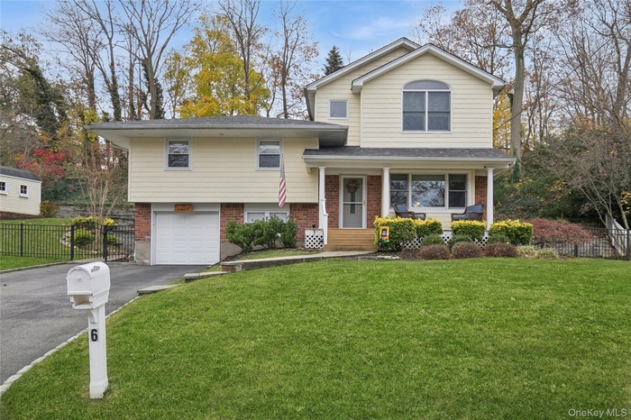 Split level home with brick siding, driveway, covered porch, an attached garage, and a shingled roof