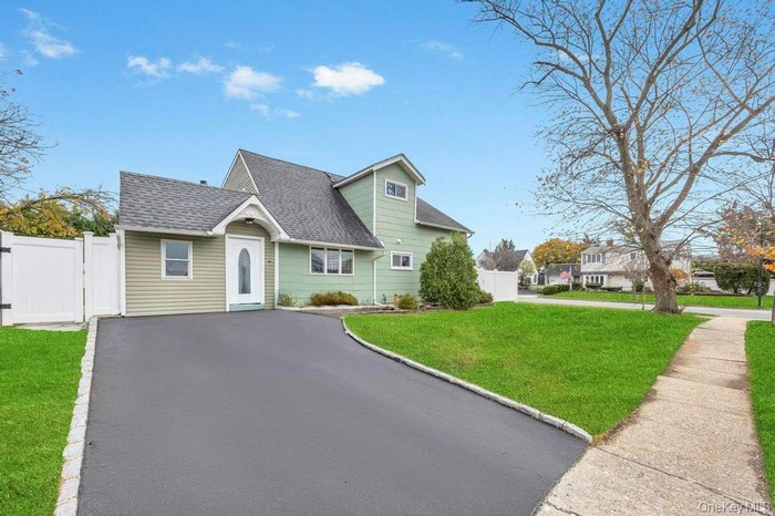 Cape cod-style house featuring roof with shingles, a gate, and asphalt driveway