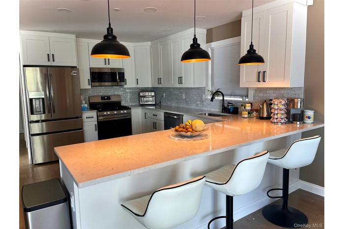 Kitchen featuring appliances with stainless steel finishes, white cabinets, and a kitchen bar