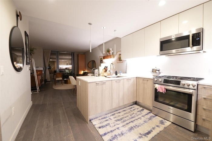 Kitchen featuring appliances with stainless steel finishes, a peninsula, modern cabinets, decorative light fixtures, and dark wood-style floors