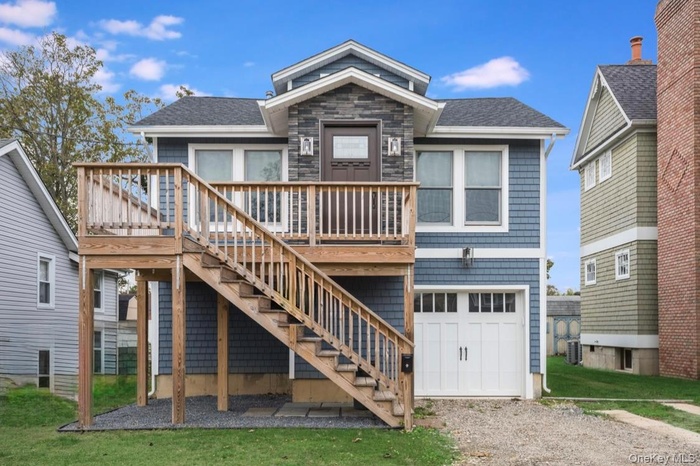 View of front facade featuring a front lawn, stairway, a deck, a garage, and roof with shingles