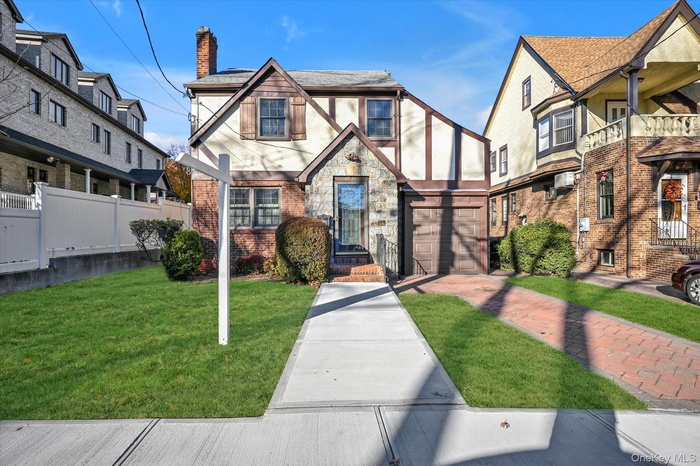 Tudor house featuring stucco siding, a chimney, a front lawn, stone siding, and brick siding