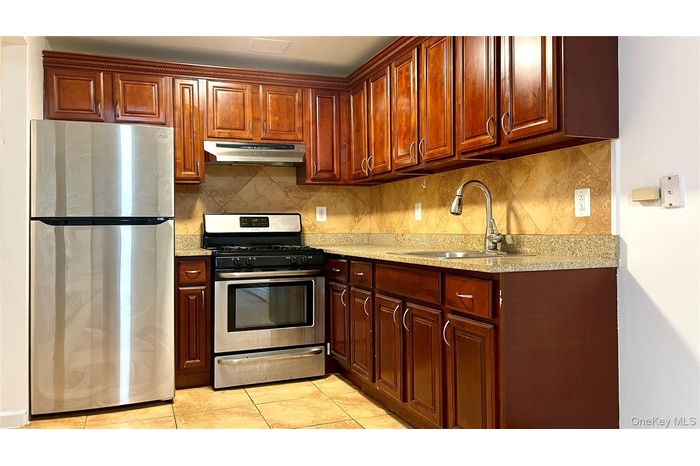 Kitchen with stainless steel appliances, light stone countertops, decorative backsplash, under cabinet range hood, and light tile patterned floors