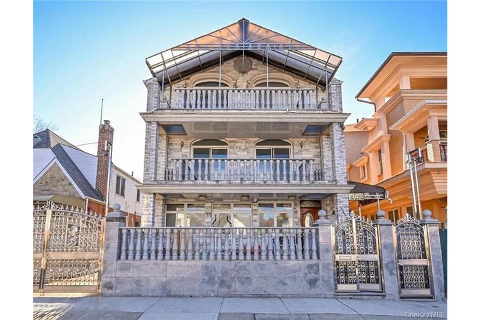 View of front of home with a balcony, stone siding, a gate, and a fenced front yard