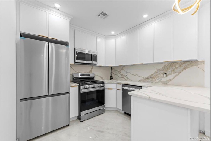 Kitchen with stainless steel appliances, light marble finish floors, white cabinets, light stone counters, and a peninsula