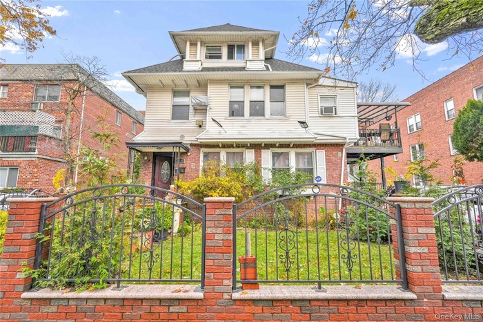 American foursquare style home featuring a shingled roof, a gate, a balcony, and brick siding