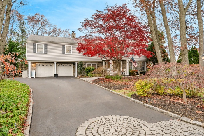 View of front home with a chimney, driveway, stone siding, and a garage