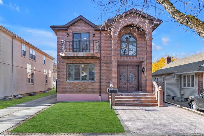 View of front facade with brick siding, a front yard, and a balcony