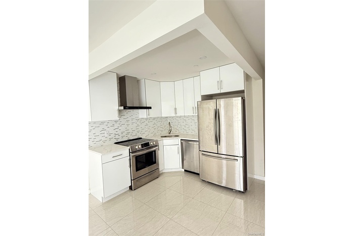 Kitchen featuring white cabinetry, appliances with stainless steel finishes, wall chimney exhaust hood, and backsplash