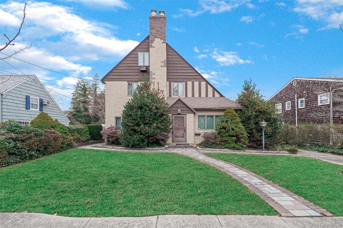 Tudor-style house featuring a front lawn and a chimney