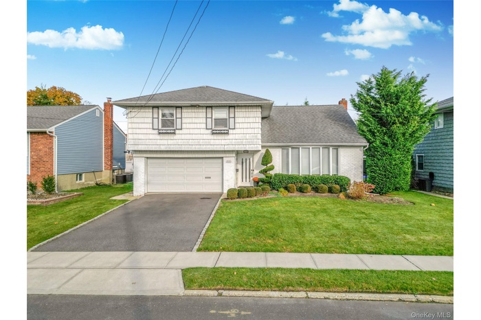 View of front of home with brick siding, a front lawn, asphalt driveway, roof with shingles, and a garage