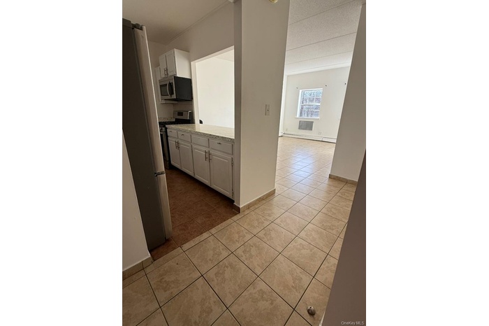 Kitchen with white cabinets, light tile patterned floors, stainless steel appliances, and baseboard heating