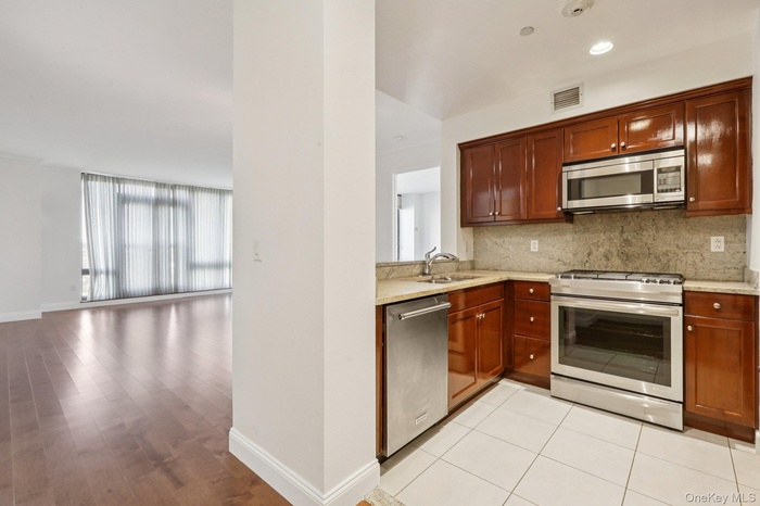 Kitchen featuring appliances with stainless steel finishes, light stone countertops, decorative backsplash, open floor plan, and light wood-style floo