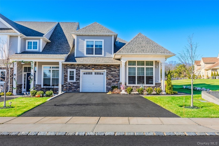 View of front of home featuring a front yard, stone siding, asphalt driveway, roof with shingles, and a porch