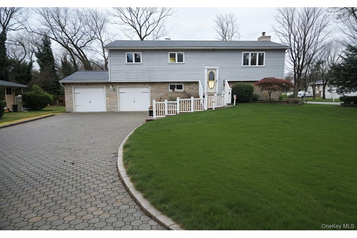 View of front facade featuring decorative driveway, stone siding, a chimney, a front lawn, and an attached garage