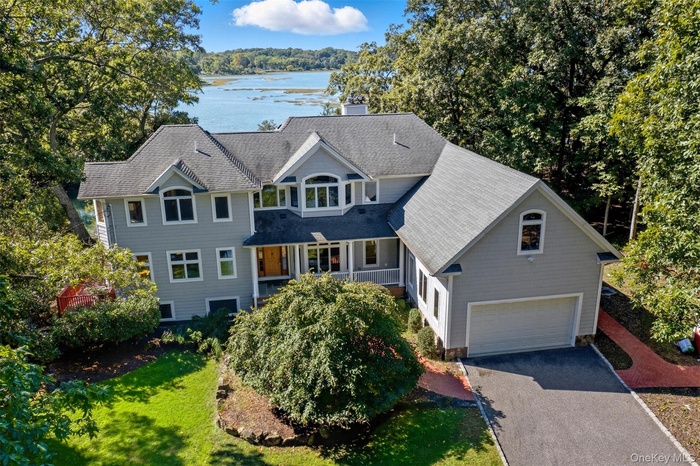 View of front of house featuring asphalt driveway, a chimney, roof with shingles, a front lawn, and a water view