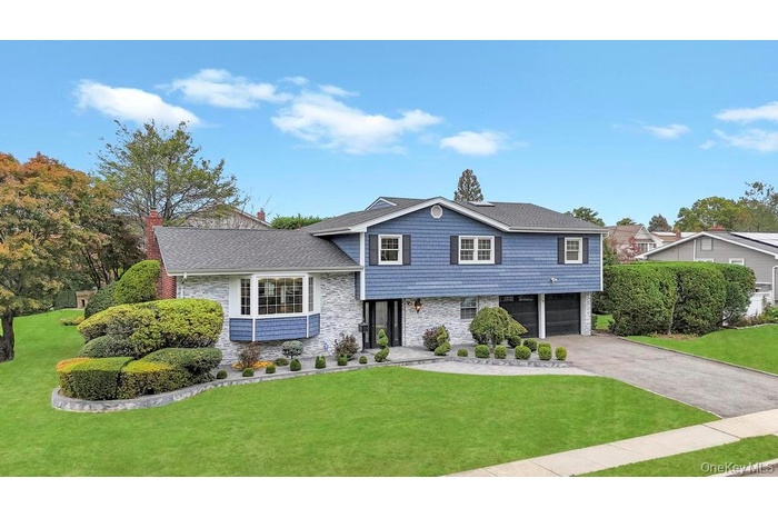 Split level home featuring a front lawn, a chimney, asphalt driveway, and an attached garage